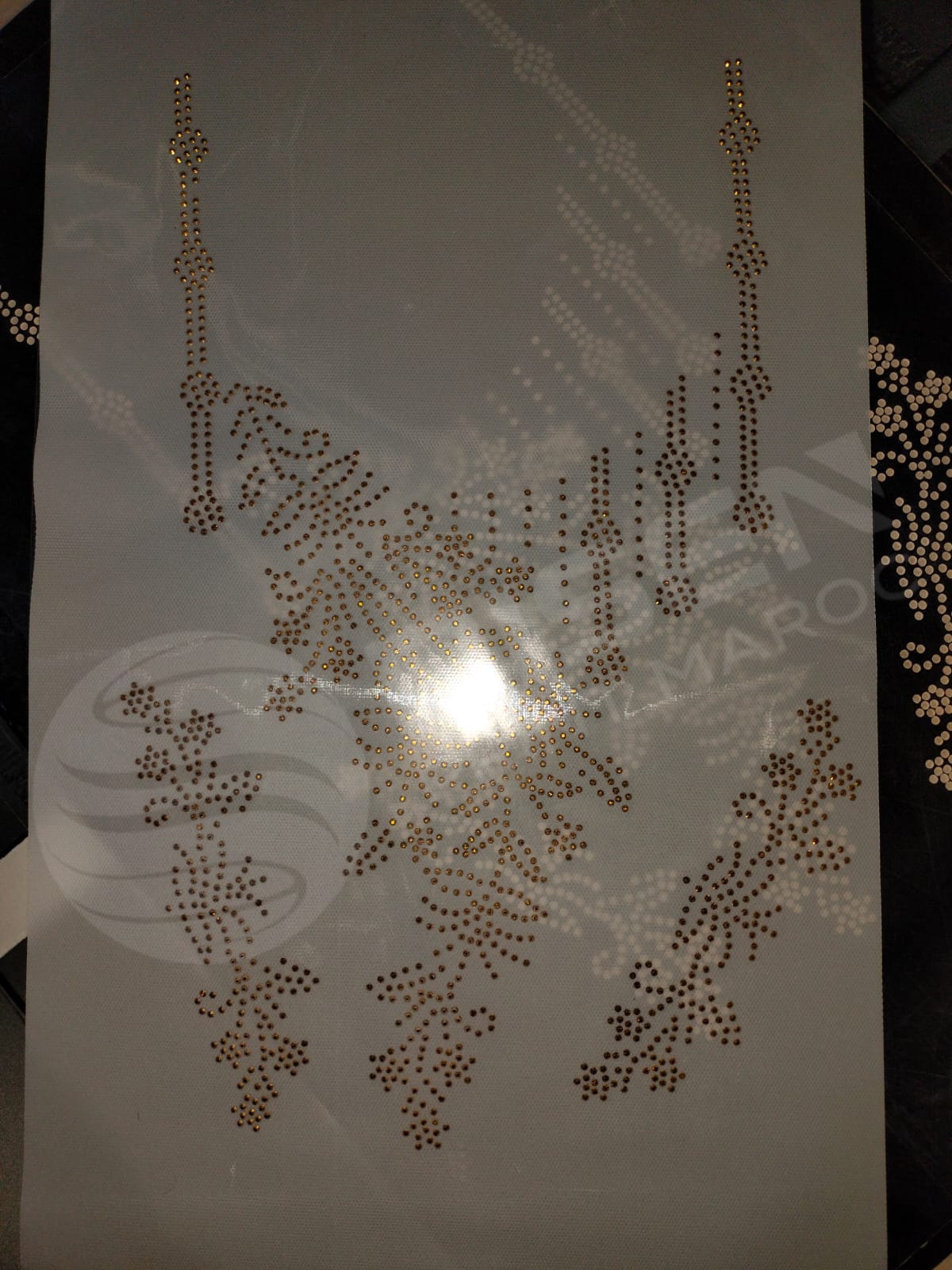 Détail d'un gabarit de strass dorés sur film de transfert transparent prêt pour la pose sur vêtement
